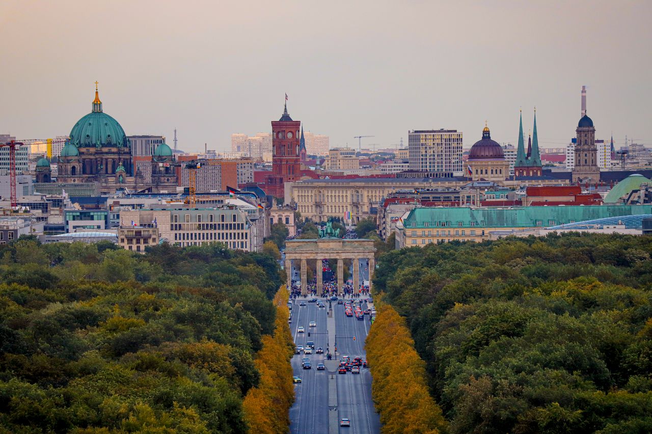 Aerial view of Berlin with a focus on Brandenburg Gate amidst urban and green landscapes.